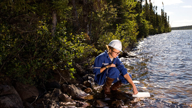 A field technician collecting a water sample from a lake downstream of a uranium mine or mill.